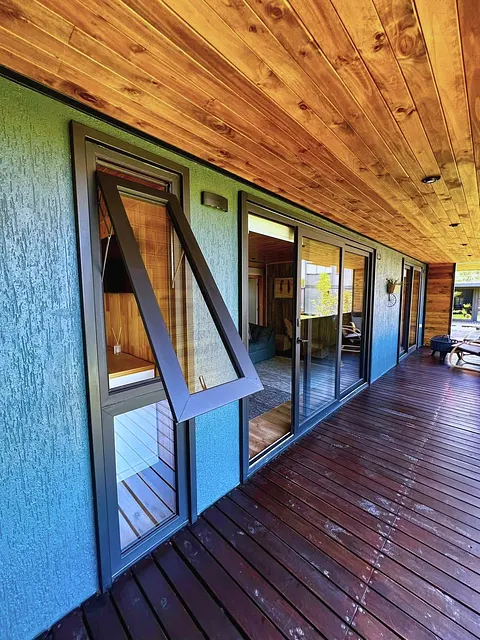 Ventana proyectante de PVC grafito abierta sobre terraza con deck