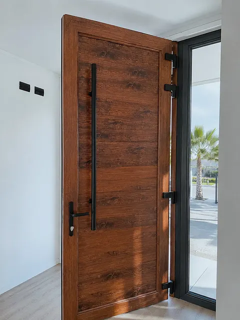 Puerta de PVC acabado nogal con manilla negra, instalada en acceso de vivienda